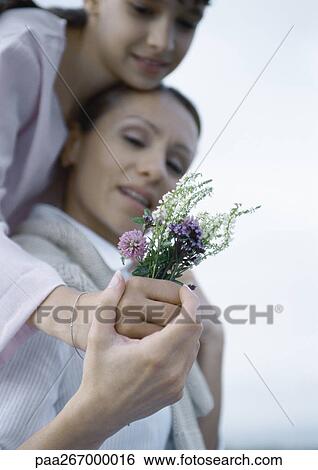 Girl embracing mother from behind, mother's hand over girl's, holding bouquet of wildflowers View Large Photo Image Stock Photograph - Girl embracing mother from behind, mother's hand over girl's, holding bouquet of wildflowers. Fotosearch