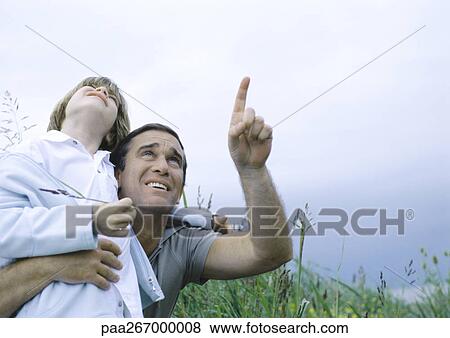 Stock Photo - Man holding son in arms pointing to overcast sky. Fotosearch