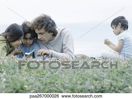 Man lying on grass with boy and girl looking at cellphone, second boy sitting apart View Large Photo Image Stock Photograph - Man lying on grass with boy and girl looking at cellphone, second boy sitting apart. Fotosearch