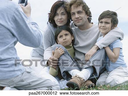 Parents with boy and girl sitting on grass posing for photo, boy taking photo View Large Photo Image Stock Image - Parents with boy and girl sitting on grass posing for photo, boy taking photo. Fotosearch