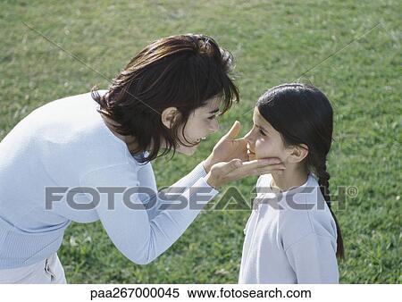 Stock Photography - Woman bending over holding daughters face between hands, side view. Fotosearch