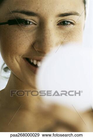 Stock Photo - Woman applying mascara, close-up, compact blurred in foreground. Fotosearch