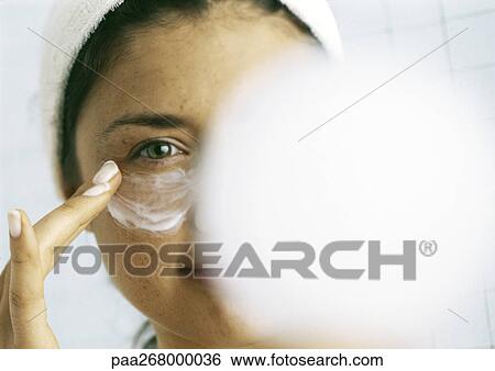 Stock Photograph - Woman applying moisturizer beneath eye, blurred compact in foreground. Fotosearch