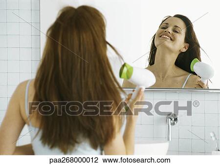 Stock Image - Woman drying hair in front of mirror. Fotosearch