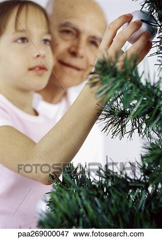 Stock Photo - Girl and grandfather decorating Christmas tree. Fotosearch