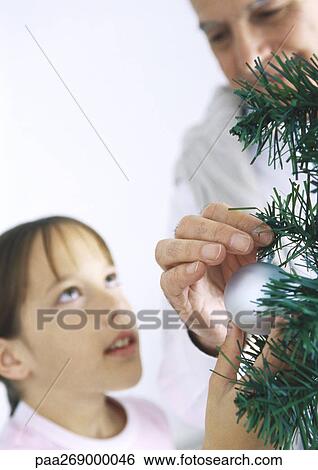 Stock Photograph - Girl and grandfather decorating Christmas tree. Fotosearch