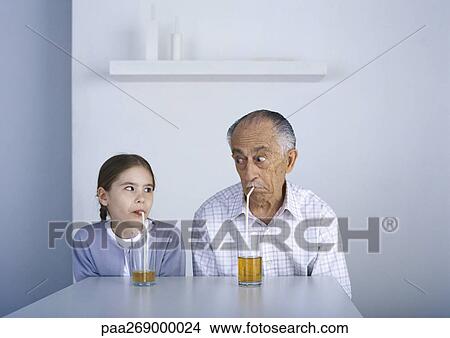 Girl and grandfather sitting at table drinking with straws View Large Photo Image Picture - Girl and grandfather sitting at table drinking with straws. Fotosearch