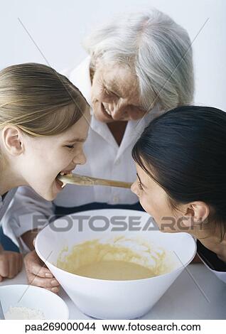 Girls tasting batter from bowl, senior woman smiling in background View Large Photo Image Picture - Girls tasting batter from bowl, senior woman smiling in background. Fotosearch