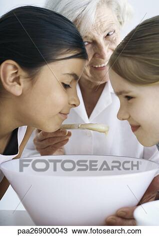 Girls with heads over bowl, senior woman holding spoon in background View Large Photo Image Stock Image - Girls with heads over bowl, senior woman holding spoon in background. Fotosearch