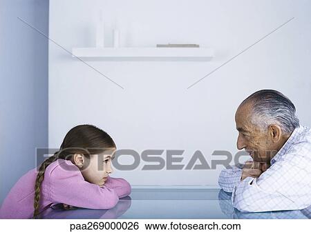 Grandfather and girl sitting with heads on table View Large Photo Image Stock Photograph - Grandfather and girl sitting with heads on table . Fotosearch