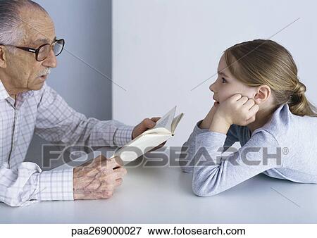 Grandfather reading book to girl, sitting at table View Large Photo Image Stock Photo - Grandfather reading book to girl, sitting at table . Fotosearch