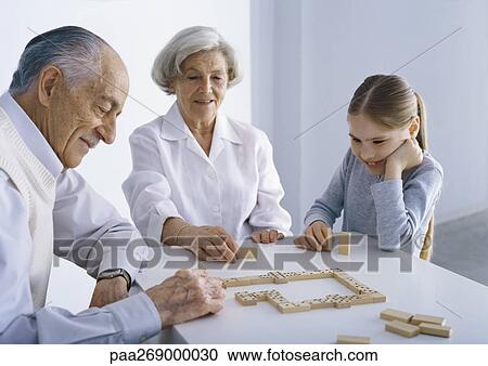 Grandparents and girl sitting at table playing dominoes View Large Photo Image Stock Image - Grandparents and girl sitting at table playing dominoes. Fotosearch