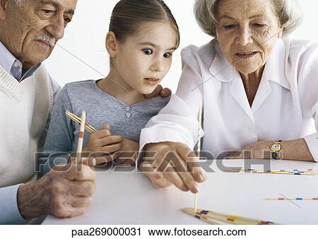 Grandparents and girl sitting at table playing pick up sticks View Large Photo Image Stock Image - Grandparents and girl sitting at table playing pick up sticks. Fotosearch