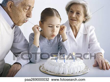 Grandparents and girl sitting at table blowing out candles on cake View Large Photo Image Stock Image - Grandparents and girl sitting at table blowing out candles on cake. Fotosearch