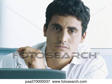 Stock Photo - Businessman holding glasses, looking at camera. Fotosearch