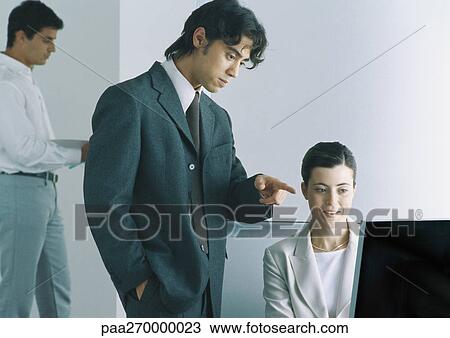 Businessman pointing at computer screen, businesswoman sitting next to him smiling, man in background View Large Photo Image Stock Image - Businessman pointing at computer screen, businesswoman sitting next to him smiling, man in background. Fotosearch
