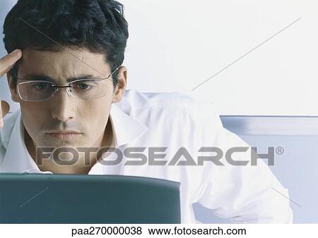 Businessman wearing glasses, furrowing brow, looking at computer screen View Large Photo Image Stock Photo - Businessman wearing glasses, furrowing brow, looking at computer screen. Fotosearch