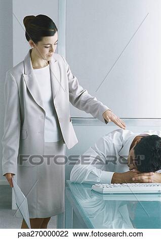 Man sitting with head down on desk, woman standing next to him tapping his shoulder View Large Photo Image Stock Image - Man sitting with head down on desk, woman standing next to him tapping his shoulder. Fotosearch