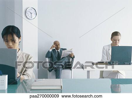 Two women working at laptops in office, businessman sitting in chair reading newspaper View Large Photo Image Stock Photo - Two women working at laptops in office, businessman sitting in chair reading newspaper. Fotosearch
