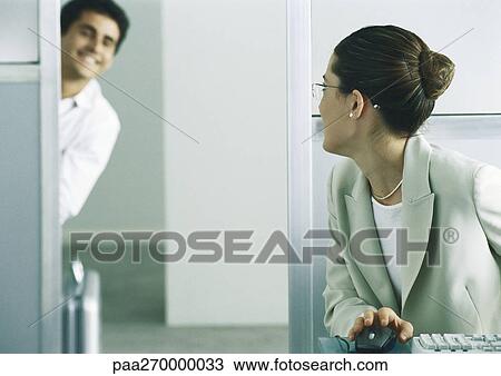 Woman sitting at desk looking over shoulder at man looking through door, smiling View Large Photo Image Stock Image - Woman sitting at desk looking over shoulder at man looking through door, smiling. Fotosearch