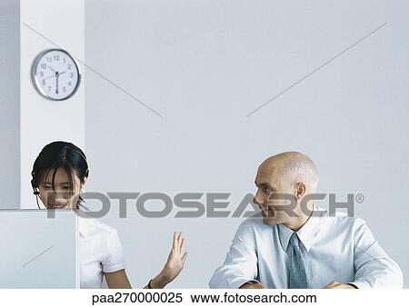 Woman sitting behind computer with headset gesturing to businessman View Large Photo Image Stock Photography - Woman sitting behind computer with headset gesturing to businessman. Fotosearch
