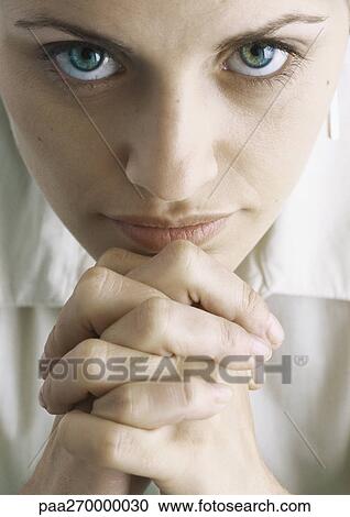 Stock Image - Woman with hands clasped looking at camera, close-up. Fotosearch