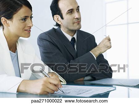 Businessman and businesswoman sitting at table with documents View Large Photo Image Stock Image - Businessman and businesswoman sitting at table with documents. Fotosearch