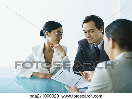 Businessman and businesswoman sitting at table across from businesswoman holding out document and pen View Large Photo Image Stock Photo - Businessman and businesswoman sitting at table across from businesswoman holding out document and pen. Fotosearch
