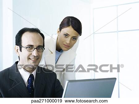 Businessman and businesswoman with laptop looking at camera View Large Photo Image Stock Photo - Businessman and businesswoman with laptop looking at camera. Fotosearch