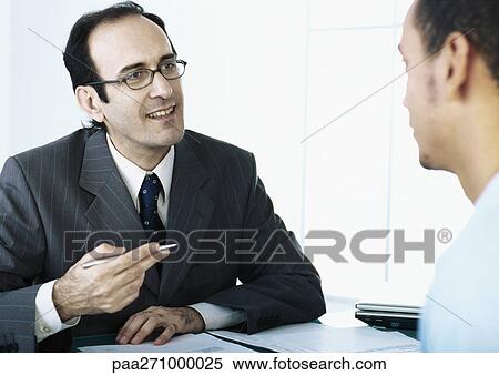 Businessman gesturing with pen in hand, speaking to man View Large Photo Image Stock Photography - Businessman gesturing with pen in hand, speaking to man. Fotosearch