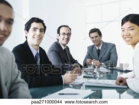 Businesspeople sitting around table, smiling at camera View Large Photo Image Picture - Businesspeople sitting around table, smiling at camera. Fotosearch