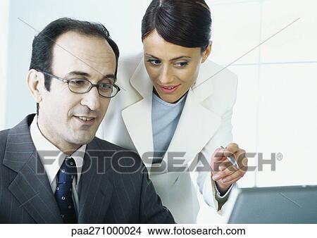 Businesswoman leaning over businessman's shoulder, pointing View Large Photo Image Picture - Businesswoman leaning over businessman's shoulder, pointing. Fotosearch