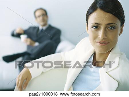 Businesswoman looking at camera, businessman with legs crosses holding cup in background View Large Photo Image Stock Photo - Businesswoman looking at camera, businessman with legs crosses holding cup in background. Fotosearch