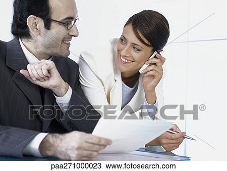 Businesswoman talking on cell phone smiling at businessman next to her View Large Photo Image Stock Image - Businesswoman talking on cell phone smiling at businessman next to her. Fotosearch