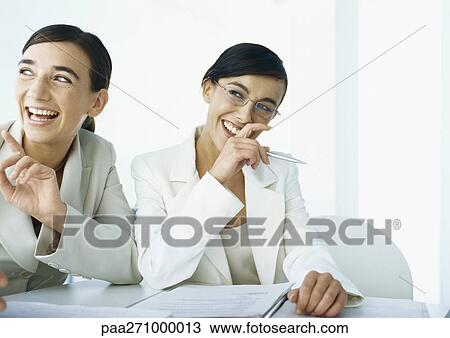 Stock Image - Two businesswomen laughing, looking to the side. Fotosearch