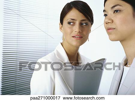 Two businesswomen standing together looking to the side View Large Photo Image Stock Photo - Two businesswomen standing together looking to the side. Fotosearch