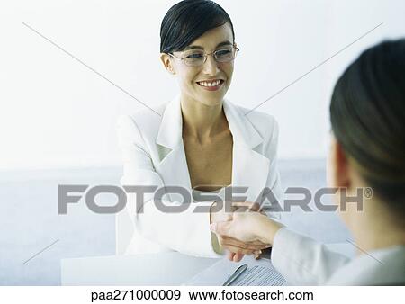 Stock Photo - Two women in suits shaking hands. Fotosearch