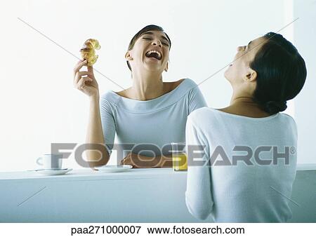 Stock Photo - Two women on either side of bar having breakfast, laughing. Fotosearch