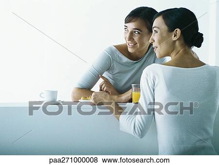 Stock Photo - Two women on either side of bar having breakfast. Fotosearch