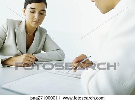 Two women sitting across from each other, one filling in application View Large Photo Image Stock Image - Two women sitting across from each other, one filling in application. Fotosearch