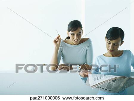 Stock Photograph - Two women taking coffee break, one reading newspaper, one smoking. Fotosearch