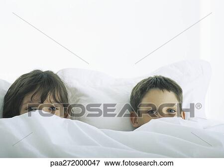 Boy and girl lying in bed, faces partially covered by duvet View Large Photo Image Stock Photo - Boy and girl lying in bed, faces partially covered by duvet. Fotosearch