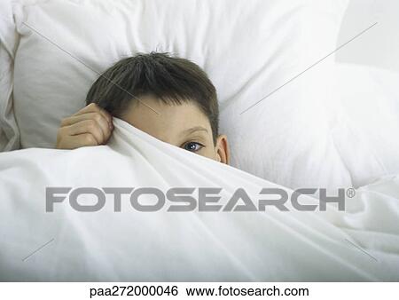 Stock Photograph - Boy in bed, peeking out behind sheet with one eye. Fotosearch