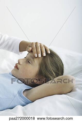 Stock Photo - Girl lying in bed with woman's hand on her forehead. Fotosearch