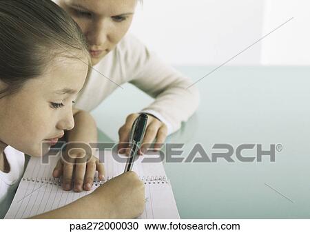 Girl sitting at table writing in notebook, woman at her side View Large Photo Image Stock Image - Girl sitting at table writing in notebook, woman at her side. Fotosearch