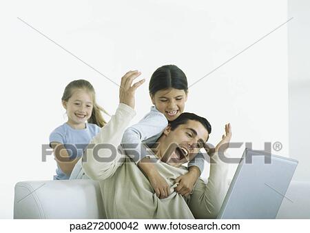 Two girls behind man sitting with laptop, one with arms around him View Large Photo Image Stock Image - Two girls behind man sitting with laptop, one with arms around him. Fotosearch