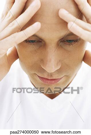 Stock Image - Man holding head, looking down, close-up. Fotosearch