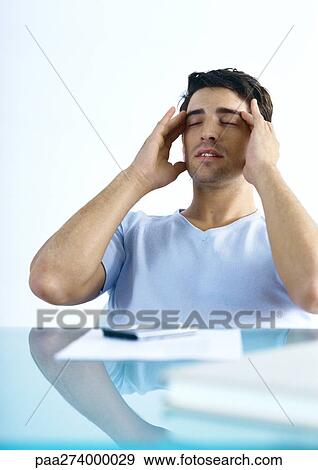 Man sitting at table, rubbing head View Large Photo Image Stock Photo - Man sitting at table, rubbing head. Fotosearch