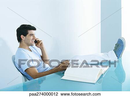 Man sitting at table with feet up, talking on phone View Large Photo Image Stock Image - Man sitting at table with feet up, talking on phone. Fotosearch