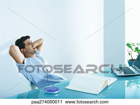 Man sitting at table with hands behind neck, listening to head phones View Large Photo Image Stock Image - Man sitting at table with hands behind neck, listening to head phones. Fotosearch